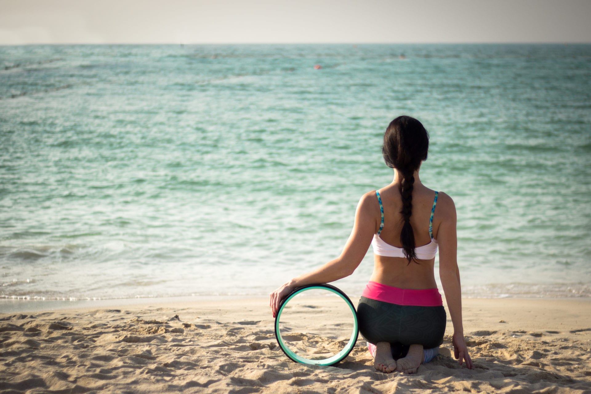 jogínka se zapletenými vlasy sedící ve vajrasaně na pláži v Dubaji, se zelenočerným yoga wheel